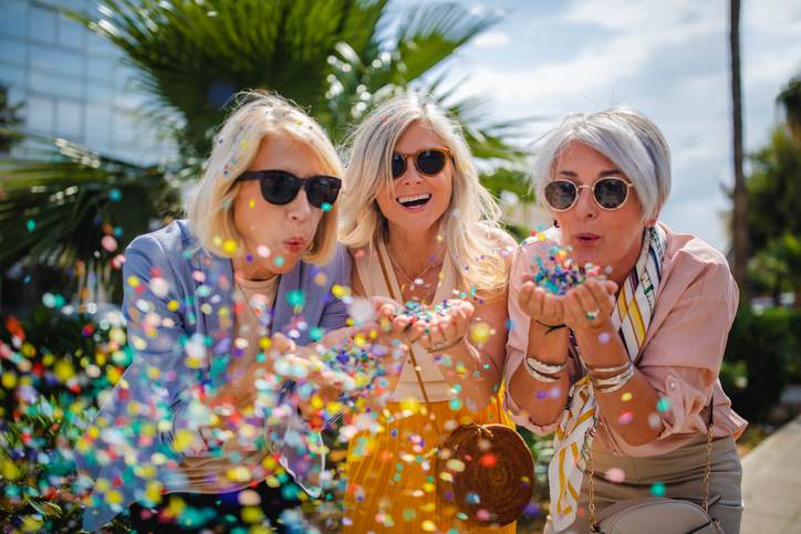 Cheerful senior women celebrating by blowing confetti in the city